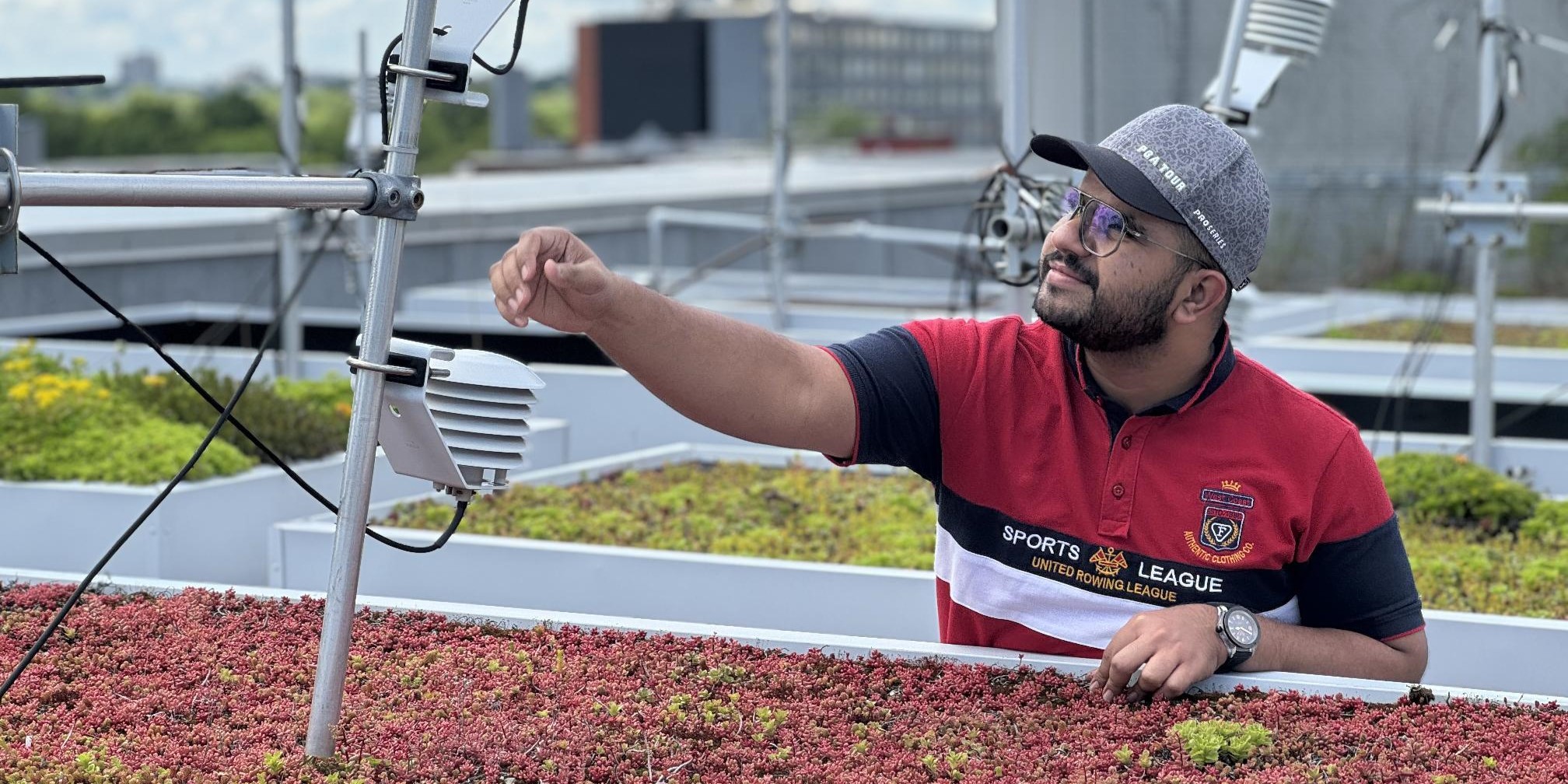Mirza reaching his arm to adjust a sensor on a metal beam on a small red sedum roof.